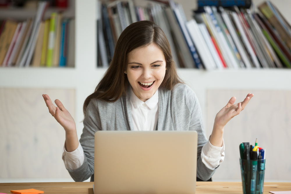 Young,Businesswoman,Looks,At,Laptop,Screen,With,Expression,Of,Joy